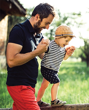 Healthy U Behavioral - Father helping toddler walk along a fence railing